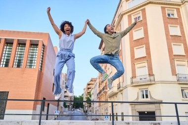 Neşeli erkek ve kadın şehirde sevinçten havalara uçuyor, başarılarını kollarını kaldırıp el ele tutuşarak kutluyorlar.