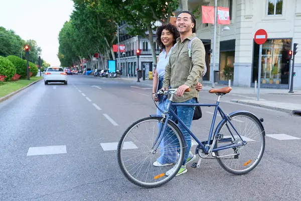 Bisikletleriyle karşıdan karşıya geçmek için bekleyen mutlu çok ırklı çift şehirde boş bir günün tadını çıkarıyor.