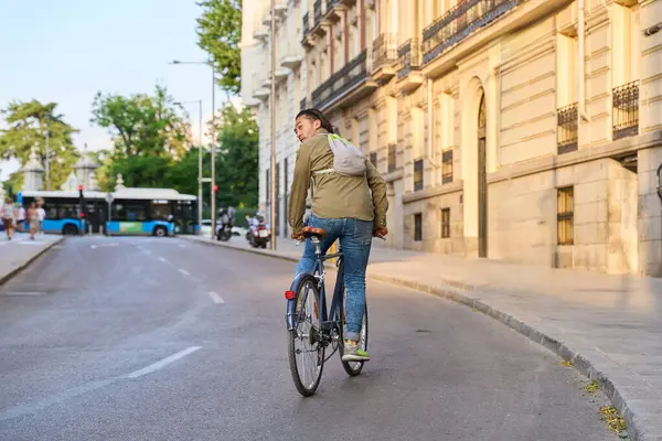 Bisikletle gezen genç bir erkek işçi güneşli bir günde şehir içi seyahatinin keyfini çıkarırken geriye bakıyor.