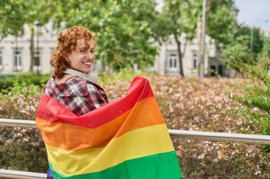 Kızıl saçlı kadın kulaklık takıyor ve gey gururuna gökkuşağı bayrağı doğrultuyor, çeşitliliği ve lgbtq artı hakları kutluyor.