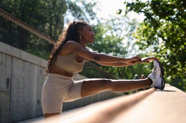 Sportif bayan koşucu sağlıklı ve aktif bir yaşam tarzını kucaklayarak canlandırıcı bir koşudan sonra şehir parkında bacak kaslarını esnetiyor.