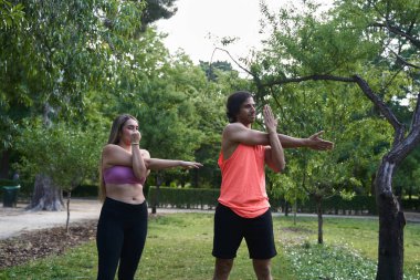 Kadın ve erkek parkta ısınıyor, egzersiz yapmadan önce kollarını esnetiyorlar.