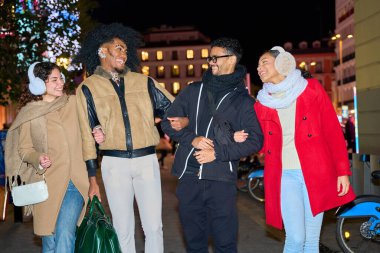 Dört arkadaş el ele yürüyorlar ve birlikte gülüyorlar. Gece bir şehir caddesinde, kış mevsiminin tadını çıkarıyorlar.