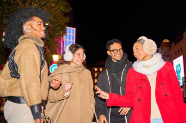 Bir grup arkadaş süslü bir şehirde kış gecesinin tadını çıkarıyor, kışlık kıyafetler giyiyor ve eğleniyorlar.