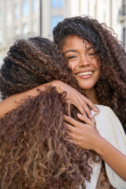 Doğal kıvırcık saçlı iki arkadaş, açık hava ortamında birbirlerine mutluluk ve destek veriyorlar.