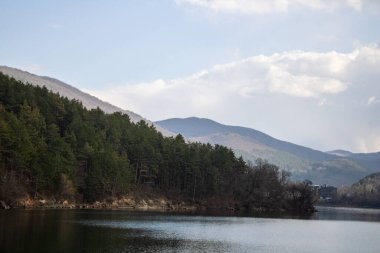 Baharda bulutlu bir ormanın arka planında bir dağ nehri olan göl.