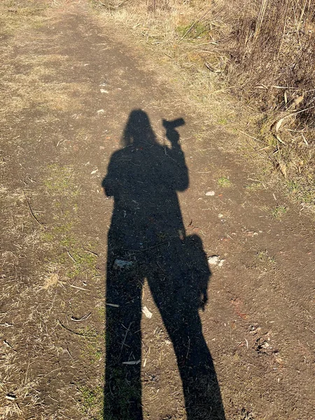 Close-up of the shadow of a person with a camera in hand and a photo bag reflecting on the ground