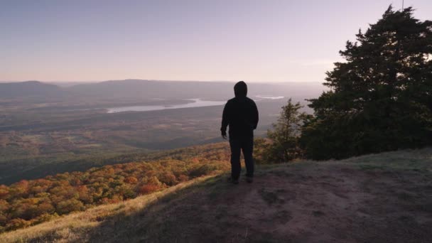 高い精神 黒いジャケットを持つ認識できない男は 秋の紅葉の谷に直面して山のピークに立って木 — ストック動画