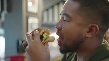 Koca ağızlı adam Austin Texas BBBQ Burger Angus Biftek Patty Mozzarella Hardal ve Patates kızartmalı Soğan halkaları yiyor.