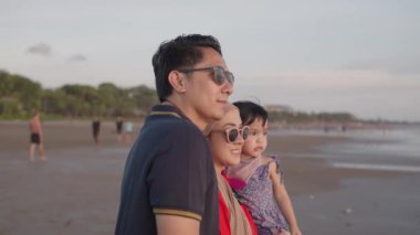 Happy Modern Muslim Southeast Asian Indonesian Family Enjoying Sunset Together on The Beach. Silhouette of Father Mother and Child in Slow Motion.