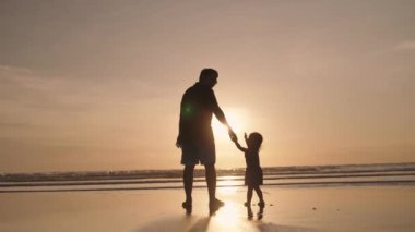 Happy Modern Muslim Southeast Asian Indonesian Family Enjoying Sunset Together on The Beach. Silhouette of Father Mother and Child in Slow Motion.