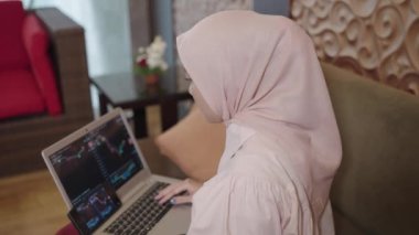 Modern Muslim Woman on Hijab Southeast Asian - Trading Investing on Stock Market Crypto Forex Through Her Laptop Displaying Graphic Chart