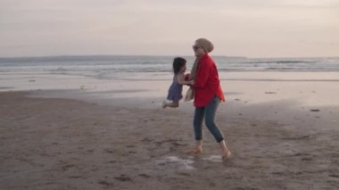 Happy Modern Muslim Southeast Asian Indonesian Family Enjoying Sunset Together on The Beach. Silhouette of Father Mother and Child in Slow Motion.