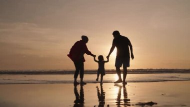 Happy Modern Muslim Southeast Asian Indonesian Family Enjoying Sunset Together on The Beach. Silhouette of Father Mother and Child in Slow Motion.