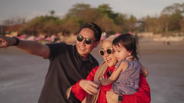幸せな現代のイスラム教徒東南アジアインドネシア家族一緒にビーチで夕日を楽しんでいます スローモーションで父と子のシルエット — ストック動画