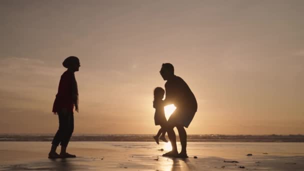 幸せな現代のイスラム教徒東南アジアインドネシア家族一緒にビーチで夕日を楽しんでいます スローモーションで父と子のシルエット — ストック動画
