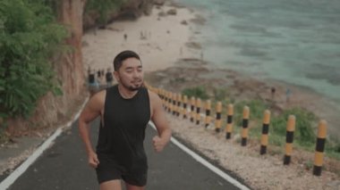 Sporty Active Man Running on The Road with White Sand Beach on the Background in Slow Motion