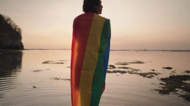 Koyu tenli Güneydoğu Asya LGBT Gay Adam Gün batımında Gökkuşağı Gurur Bayraklarıyla Sahilde Dans Ediyor