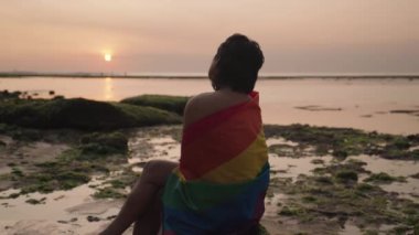 Koyu tenli Güneydoğu Asya LGBT Gay Adam Gün batımında Gökkuşağı Gurur Bayraklarıyla Sahilde Dans Ediyor