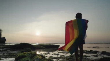 Koyu tenli Güneydoğu Asya LGBT Gay Adam Gün batımında Gökkuşağı Gurur Bayraklarıyla Sahilde Dans Ediyor