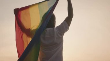 Koyu tenli Güneydoğu Asya LGBT Gay Adam Gün batımında Gökkuşağı Gurur Bayraklarıyla Sahilde Dans Ediyor