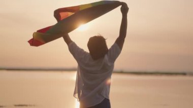 Koyu tenli Güneydoğu Asya LGBT Gay Adam Gün batımında Gökkuşağı Gurur Bayraklarıyla Sahilde Dans Ediyor