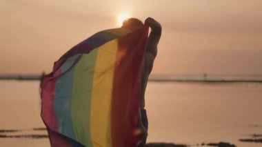 Koyu tenli Güneydoğu Asya LGBT Gay Adam Gün batımında Gökkuşağı Gurur Bayraklarıyla Sahilde Dans Ediyor