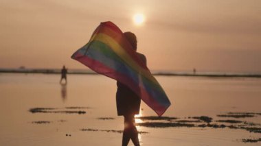 Koyu tenli Güneydoğu Asya LGBT Gay Adam Gün batımında Gökkuşağı Gurur Bayraklarıyla Sahilde Dans Ediyor