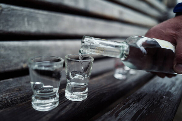 pouring vodka in a glass on wooden bench