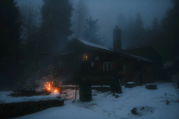 森の小さな家の近くでキャンプファイヤーを燃やしています 美しい雪の冬の夜 — ストック写真