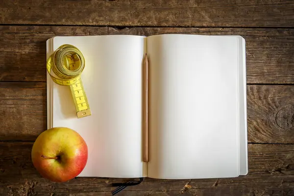 top view of a notebook and a measuring tape on a black wooden table, healthy diet, weight loss concept.
