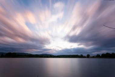Arka planda bulutlu bir günbatımı olan güzel bir göl görüntüsü.
