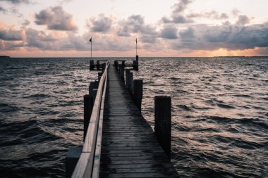 Güneşin doğuşunun güzel manzarası bulutlu ve denizde ahşap iskeleli.