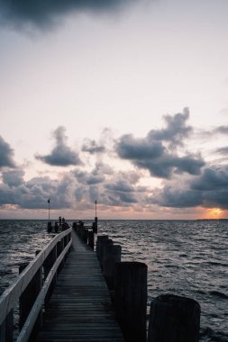 Güneşin doğuşunun güzel manzarası bulutlu ve denizde ahşap iskeleli.