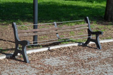 Parkta metal çerçeveli, kurumuş yapraklar ve molozlarla çevrili kırık ahşap bir bank.