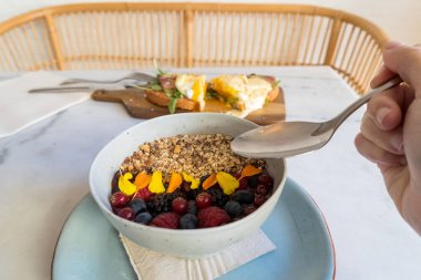 Mısır gevreği, farklı böğürtlen ve yenilebilir çiçekli tipik Brezilya aa kasesi ve arka planda haşlanmış yumurta ve jambonlu tost kahvaltısı. Mükemmel bir branç resmi..