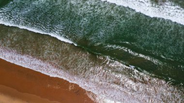 Goa deniz dalgalarının kumlu sahil şeridinde kırılışının kusursuz güzel görüntülerinin insansız hava aracı görüntüsü. Derin mavi okyanus suyu ve köpüklü dalgalarla dolu altın plaj.