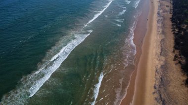 Goa deniz dalgalarının kumlu sahil şeridinde kırılışının kusursuz güzel görüntülerinin insansız hava aracı görüntüsü. Derin mavi okyanus suyu ve köpüklü dalgalarla dolu altın plaj.