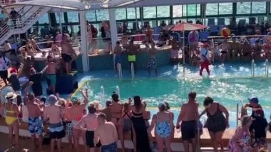 Belly Flop competition on a cruise ship. Crowds of people cheer as a large man belly flops into a cruise pool on a sunny day.