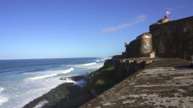 Castillo San Felipe del Morro or el Morro in San Juan, Puerto Rico. Crashing waves at fortress by the sea. Flags of colonial Spain, Puerto Rico, and United States. WWII modifications to Spanish fort.