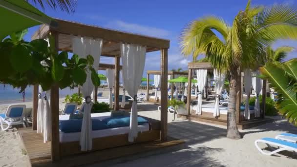 カリブ海を見下ろすビーチ カバナ 日陰でリラックスしてください ビーチ ラウンジャー カーテン ヤシの木 ビーチベッド アドレナリンビーチ ラバディ — ストック動画