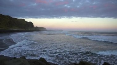 Black Sand Beach Vik, İzlanda 'da gün batımı. Reynisdrangar kayalıkları ve deniz yığınları. Vik 'in çevresindeki uçurumların ve taş yığınlarının manzarası.. 