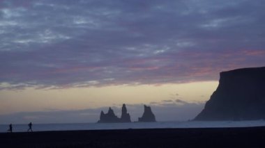 Black Sand Beach Vik, İzlanda 'da gün batımı. Reynisdrangar kayalıkları ve deniz yığınları. Vik 'in çevresindeki uçurumların ve taş yığınlarının manzarası.. 