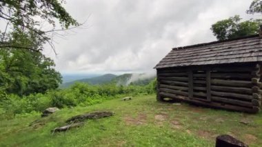 Log settler's cabin built by W. J. Trail at the Smart View Recreation Area on the Blue Ridge Parkway. Low rolling clouds on Appalachian Mountains. Pioneer dwelling of one room built in early 1890s.