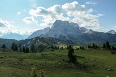 A panoramic view on the high Italian Dolomites from the top of Strudelkopf. There is a wide gravelled path leading to the top. Sunny day. A few clouds above the high peaks. Lush green plateau around