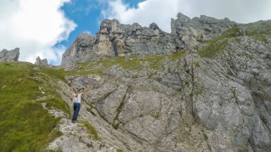 A backpacker woman hiking through Austrian Alps to the top of Hochkogel. She is walking across a landslide area. High and sharp mountains are shrouded with thick fog. Outdoor activities. Roaming free