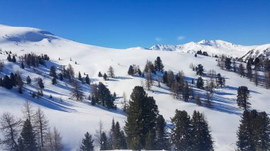 A panoramic view on the snow covered ski runs of Innerkrems, Austria. The slopes are ready for skiing. Cloudless, blue sky. A few trees overgrowing the slopes. Winter wonderland. Fresh, powder snow.