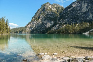 A view on the Pragser Wildsee, a lake in South Tyrolean Dolomites. High mountain chains around the lake. The sky and mountains are reflecting in the lake. Dense forest at the shore. Autumn vibe. Relax