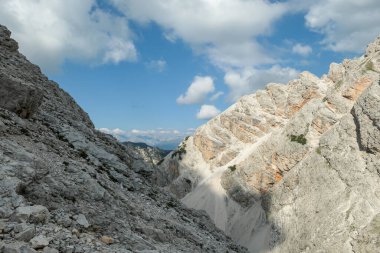 A panoramic view on a stony valley in Italian Dolomites. There are high and sharp mountains around. A narrow pathway leading through the stones. Remote and raw landscape. Sunny day. A bit of overcast