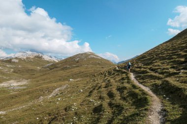 A narrow pathway along a high plateau in Italian Dolomites. Stony landscape, with a bit of green grass. High mountain chains in the back. Desolated and remote landscape. Natural habitat. A few clouds